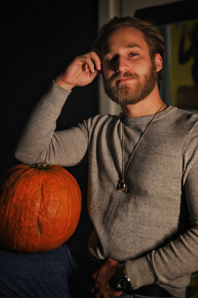 Man in a grey sweater leaning next to a pumpkin in warm evening light