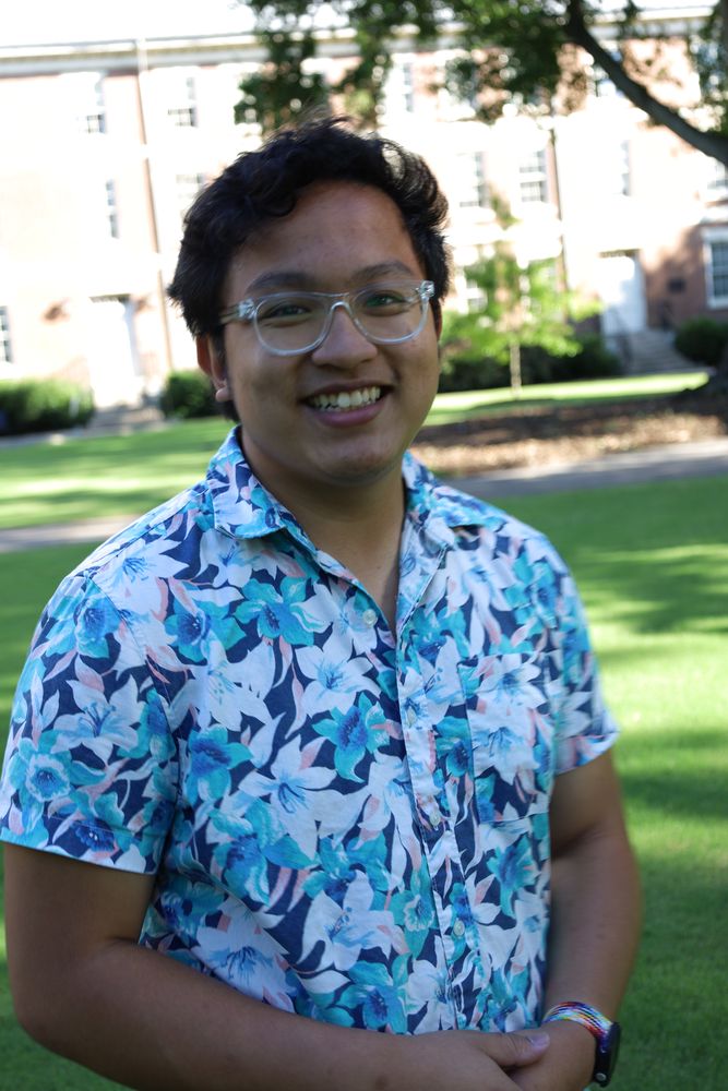 Man in a blue floral shirt smiling on the campus lawn