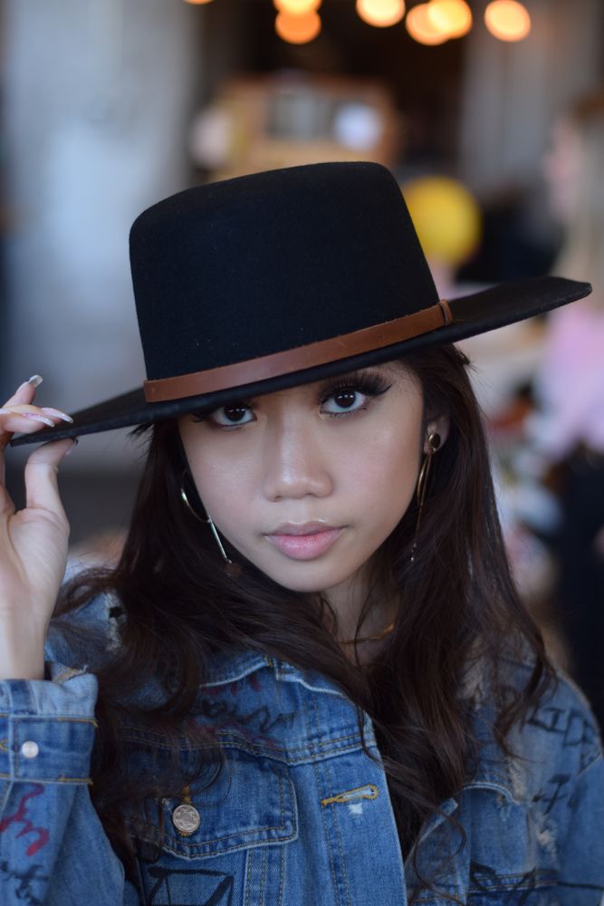 Woman in a black hat and denim jacket under warm lights