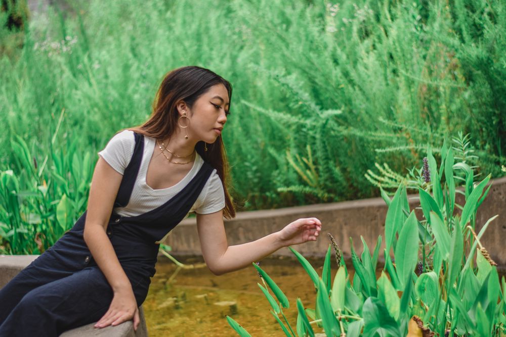 Woman in overalls sitting beside a pond with tall grasses