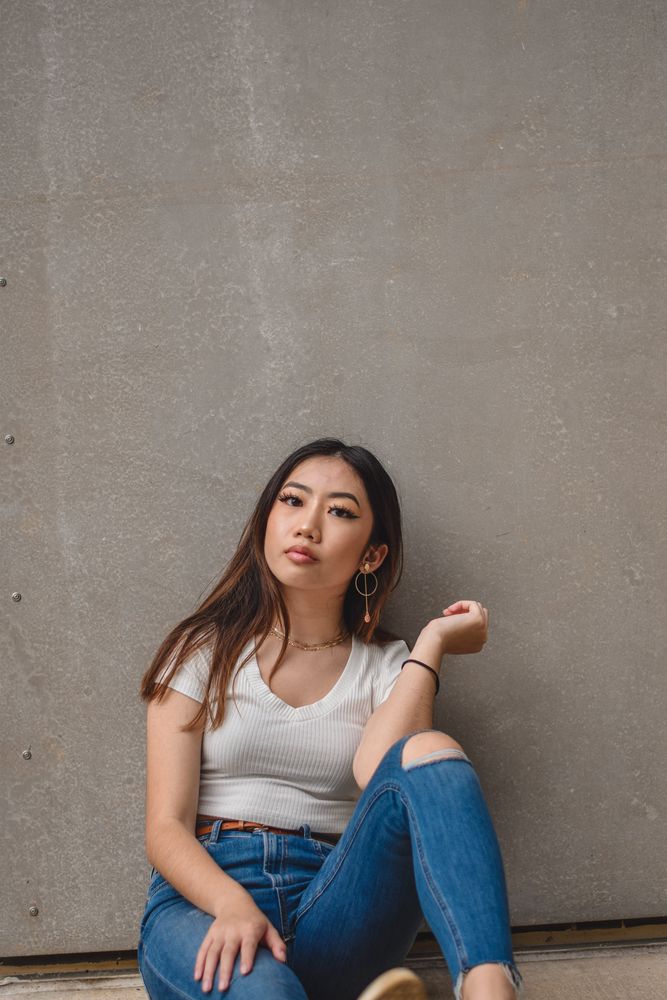 Woman in a white tee and jeans sitting against a concrete wall