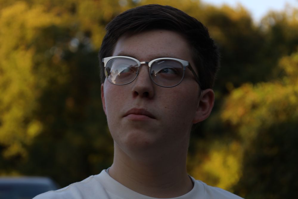 Young man in glasses against golden backlit trees