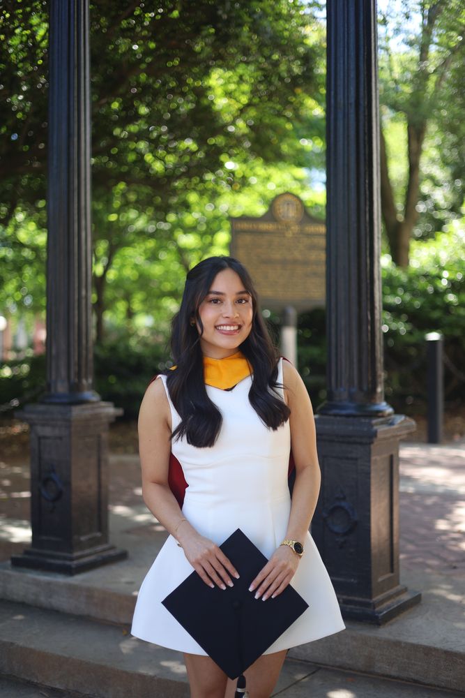 Graduate in white holding her cap under the Arch