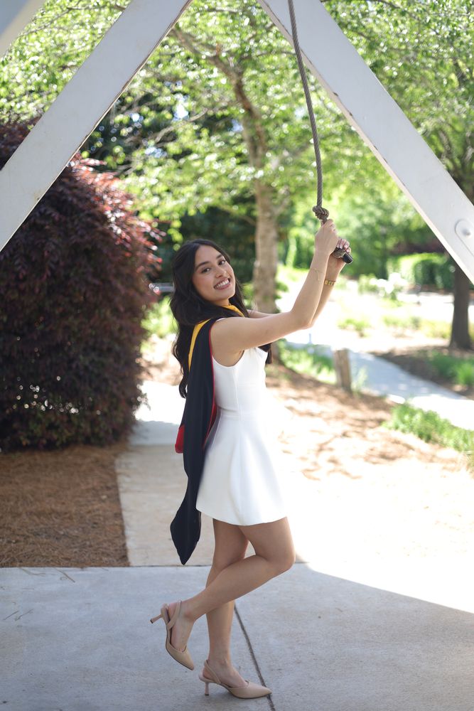 Graduate in white sitting on a swing under a white trellis