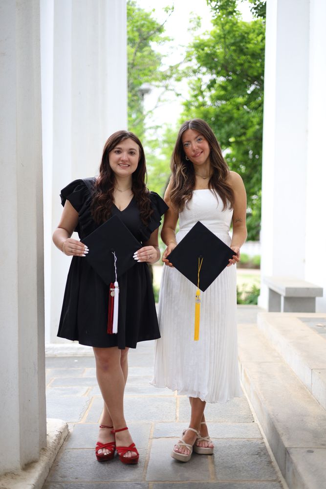Two graduates holding hands between columns
