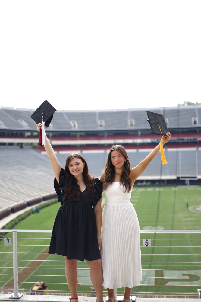 Two graduates tossing their caps in a stadium