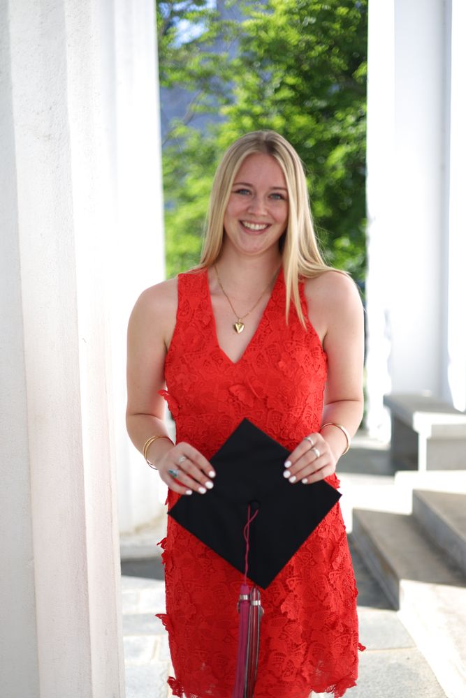 Graduate in a red dress holding her cap between white columns
