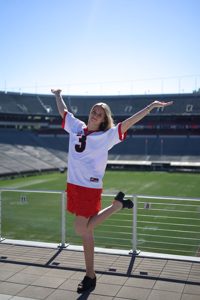Graduate in a jersey with arms raised in an empty stadium