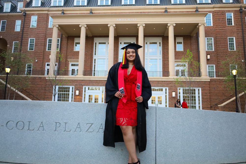 Graduate in cap and gown in front of a brick building with columns