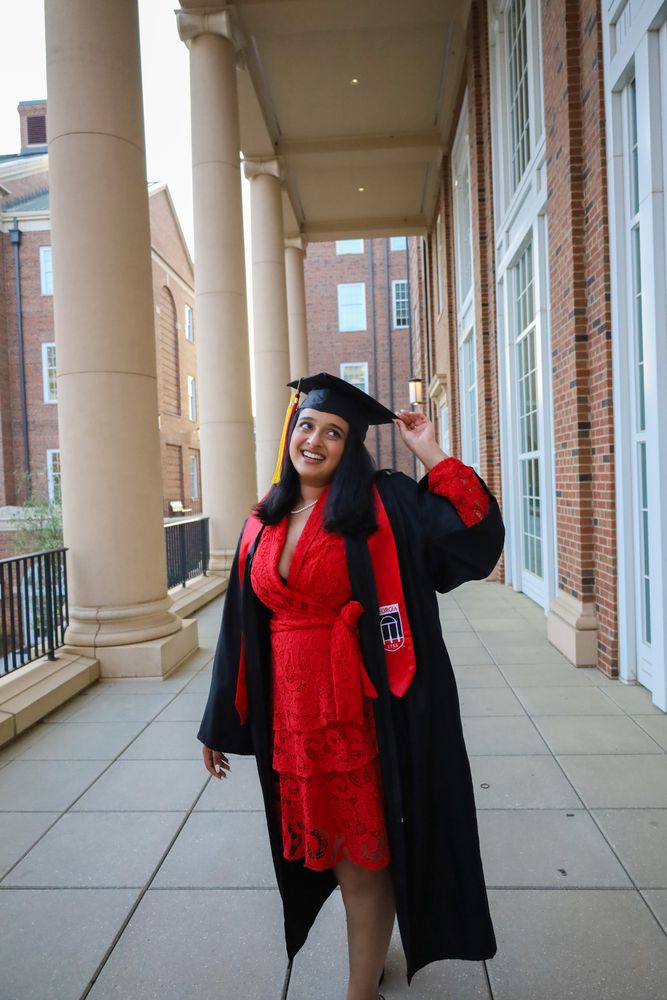 Graduate in gown and red stole between columns