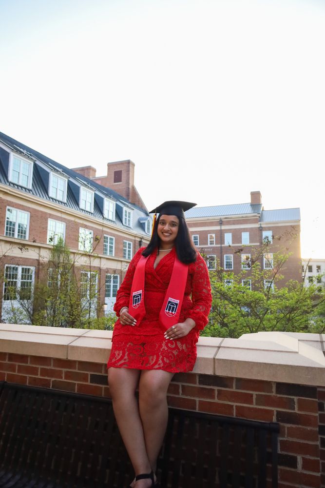 Graduate seated on a brick wall with campus buildings behind