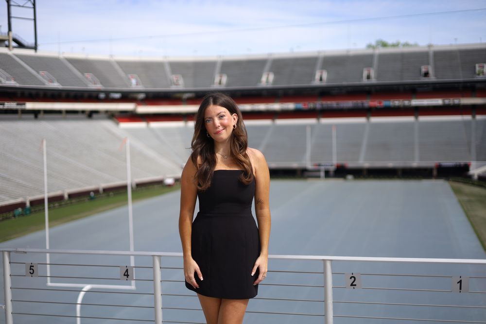 Graduate in a black dress standing in an empty stadium