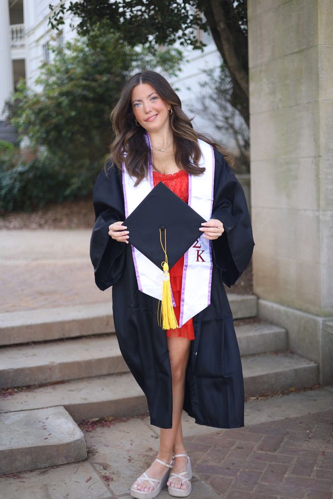 Graduate in cap and gown sitting on steps