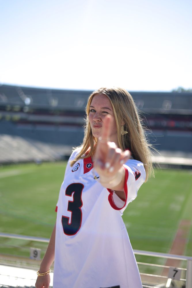 Graduate in a number 3 jersey pointing at the camera in a stadium