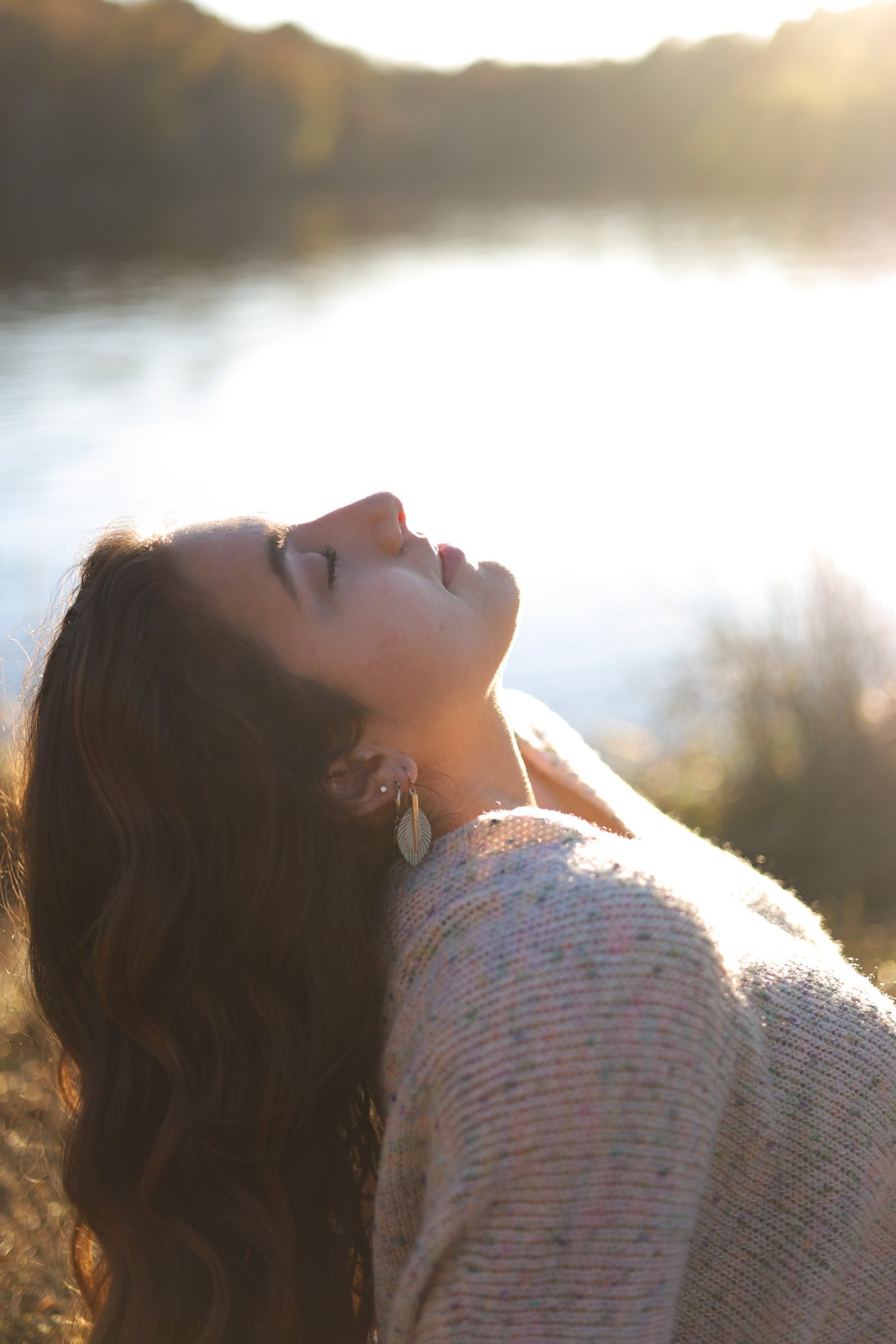 Woman tilting her head back into golden light beside a lake