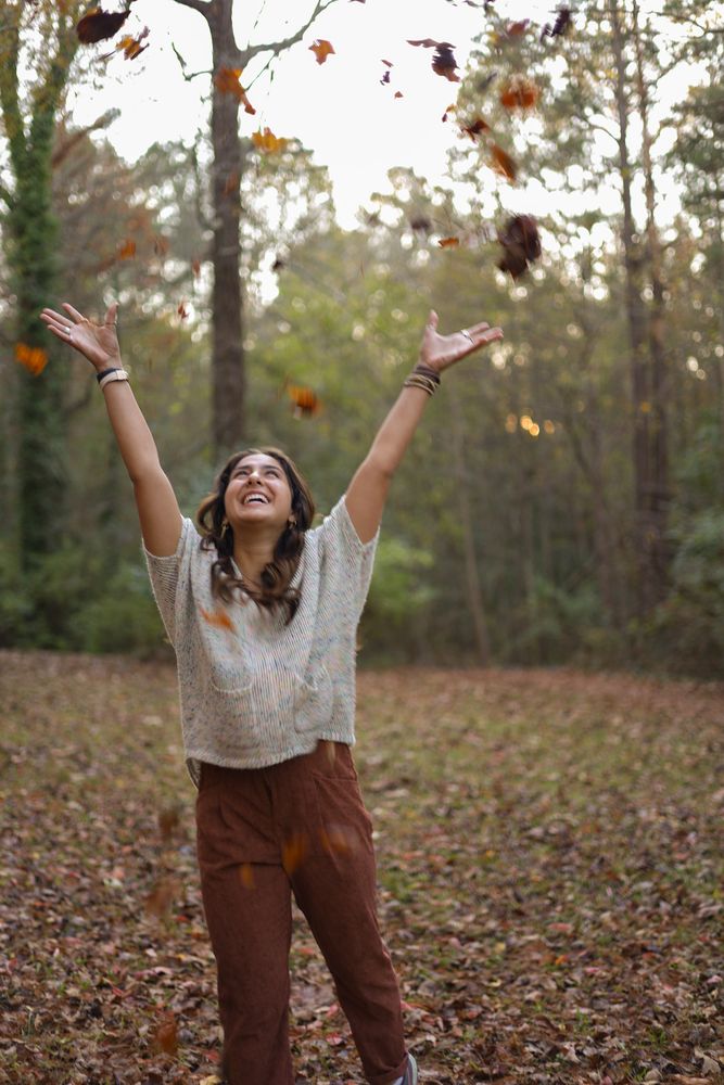 Woman throwing autumn leaves into the air in the woods