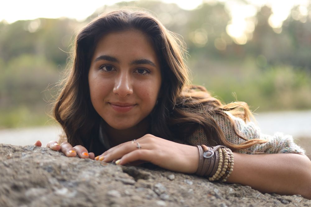 Smiling woman resting her chin on a rock by the water