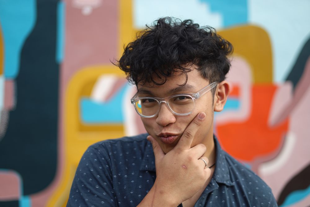Man in glasses with his hand on his chin against a mural