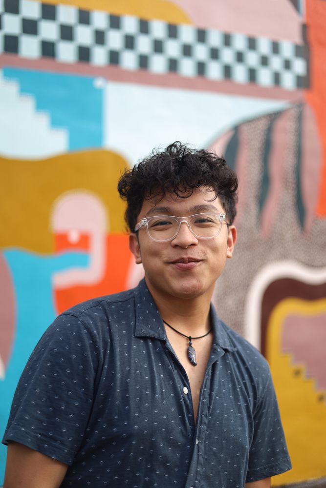 Smiling man in glasses in front of a colorful mural