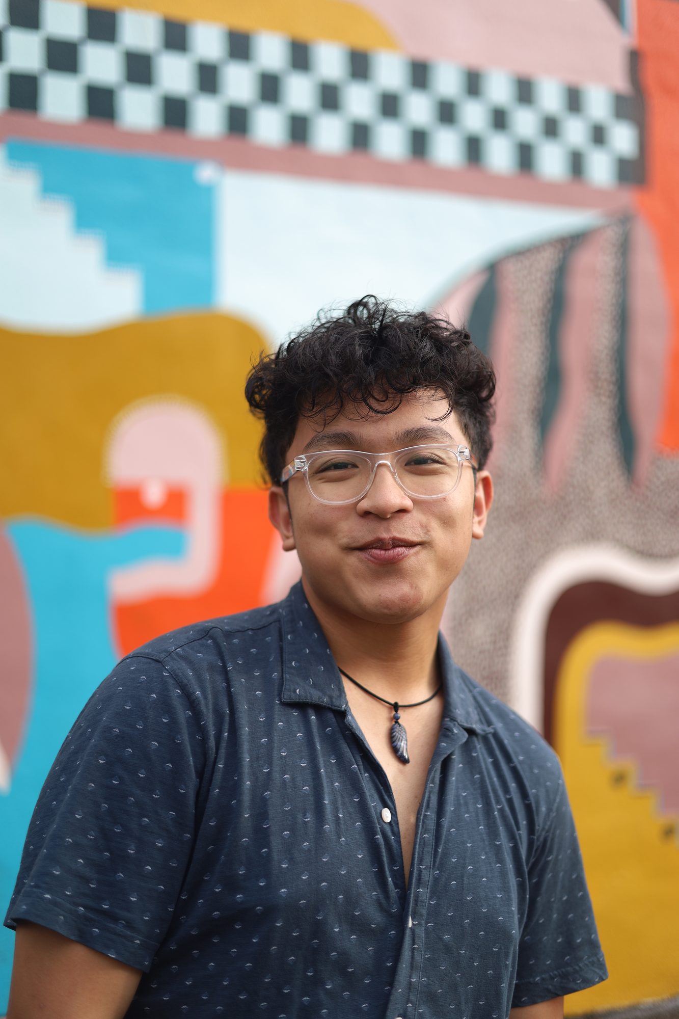 Smiling man in glasses in front of a colorful mural