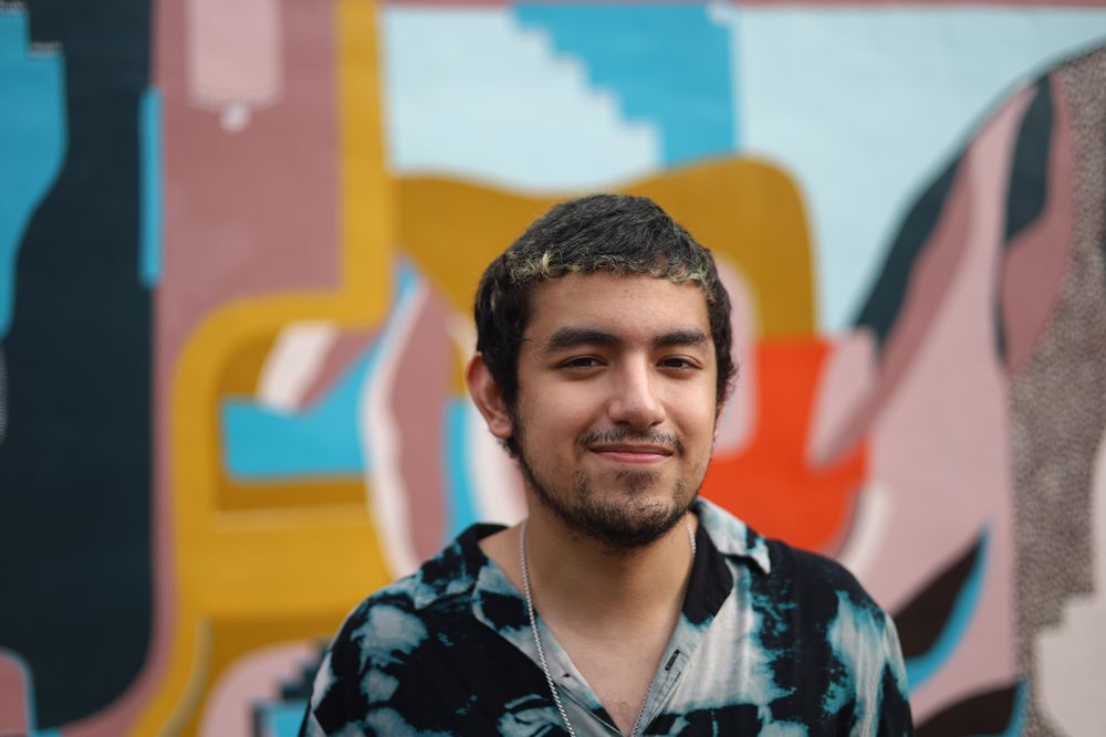 Close portrait of a smiling man in a tie-dye shirt against a mural
