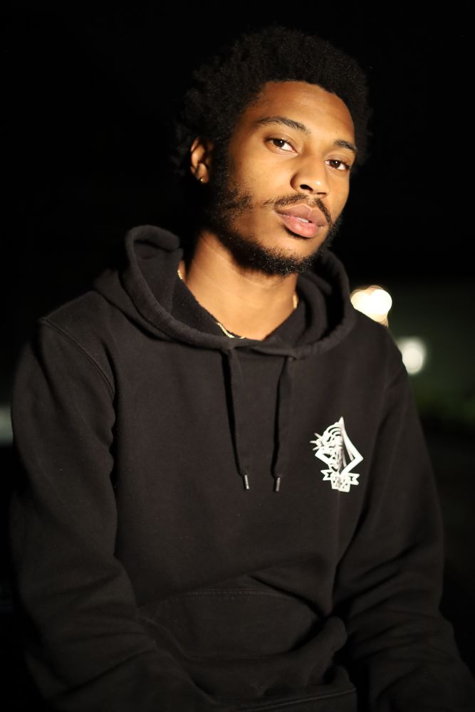 Man in a black hoodie lit by a single light at night