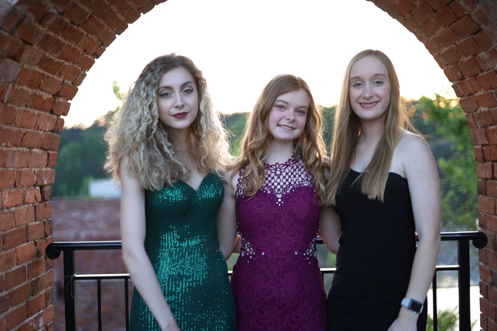 Three friends in gowns framed by a brick arch