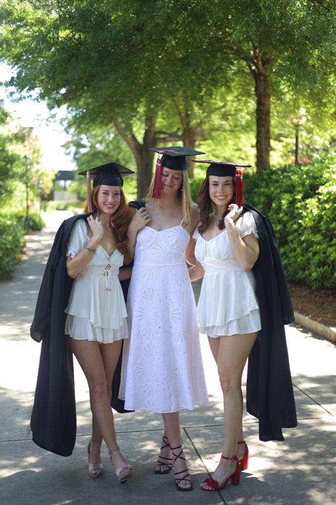Three graduates in caps walking up a tree-lined path