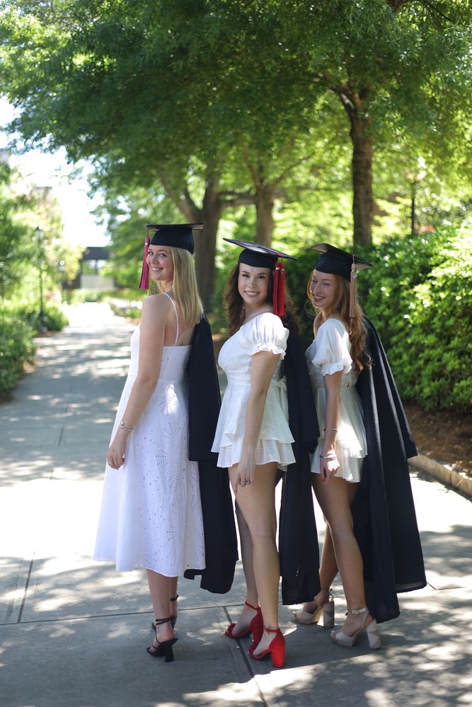 Three graduates in caps in the shade of a campus path