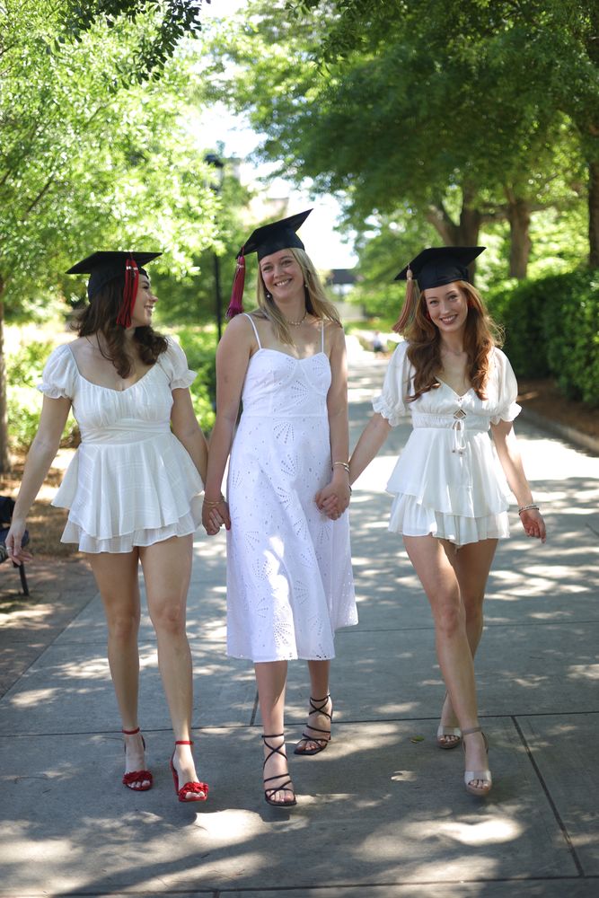 Three graduates in caps and white dresses walking down the path