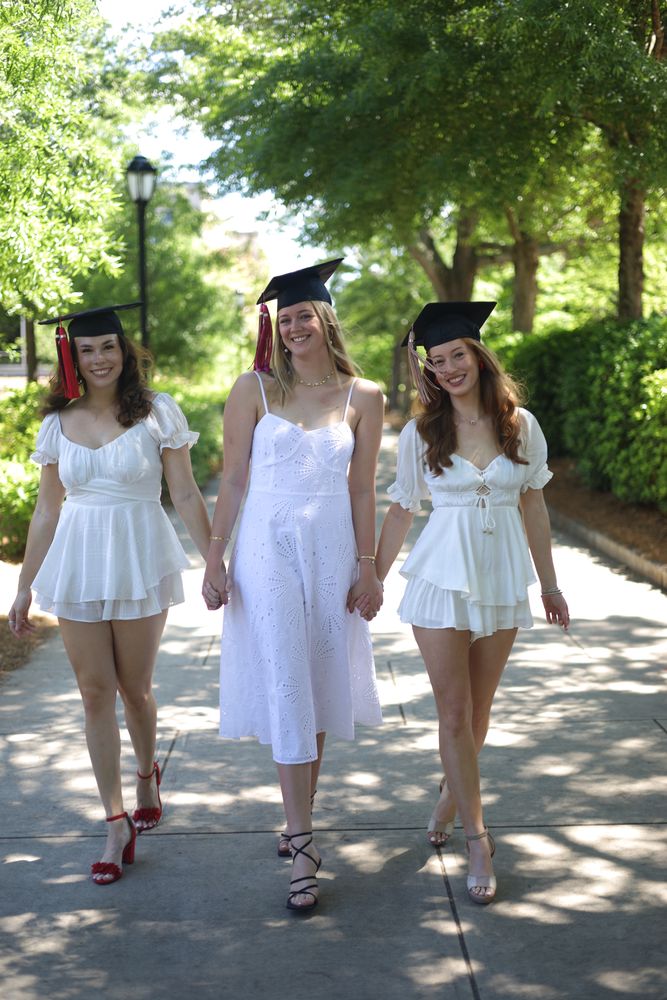 Three graduates walking toward the camera under the trees