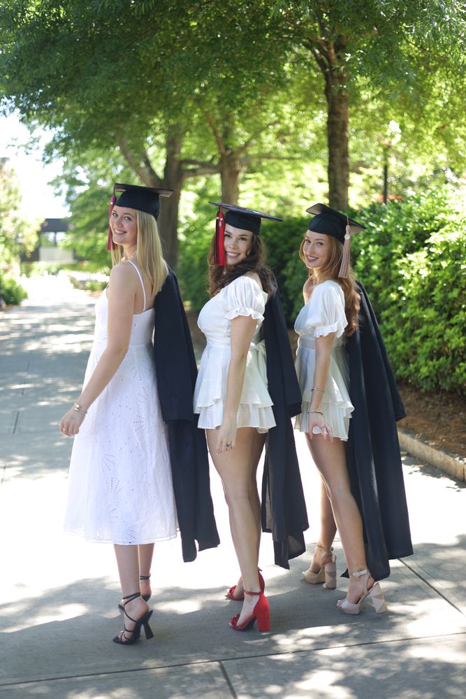 Three graduates in caps and white dresses on a tree-lined path