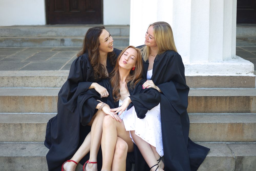 Three friends in gowns leaning into each other on the steps