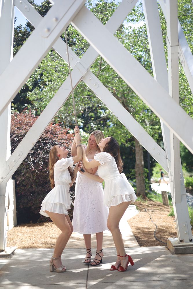 Three friends in white dresses under a white trellis