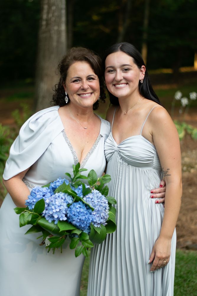 Bride with her daughter holding a blue hydrangea bouquet under the pines