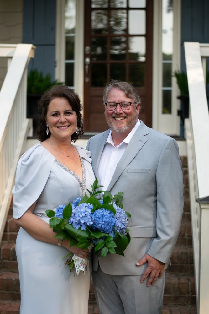 Newlyweds on the front steps holding a blue hydrangea bouquet